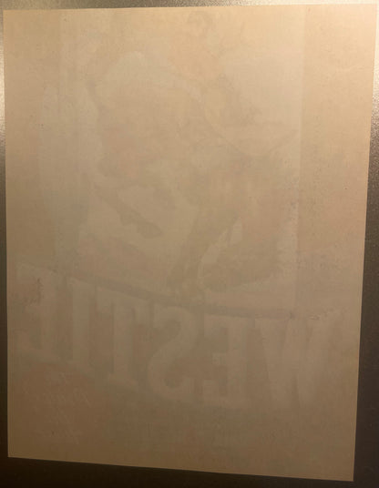 Cream-colored vintage crate label with faint printed cowboy and bucking bronco design, photographed flat against gray surface