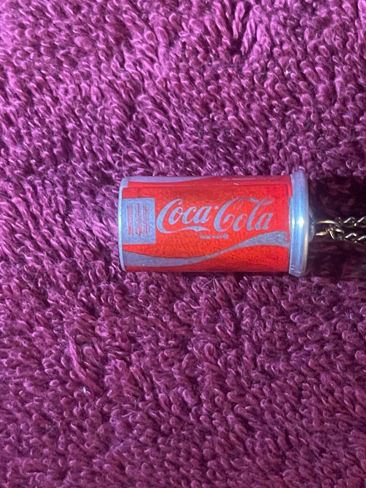 Vintage Coca-Cola mini can necklace with red label and silver script logo on purple textured fabric background
