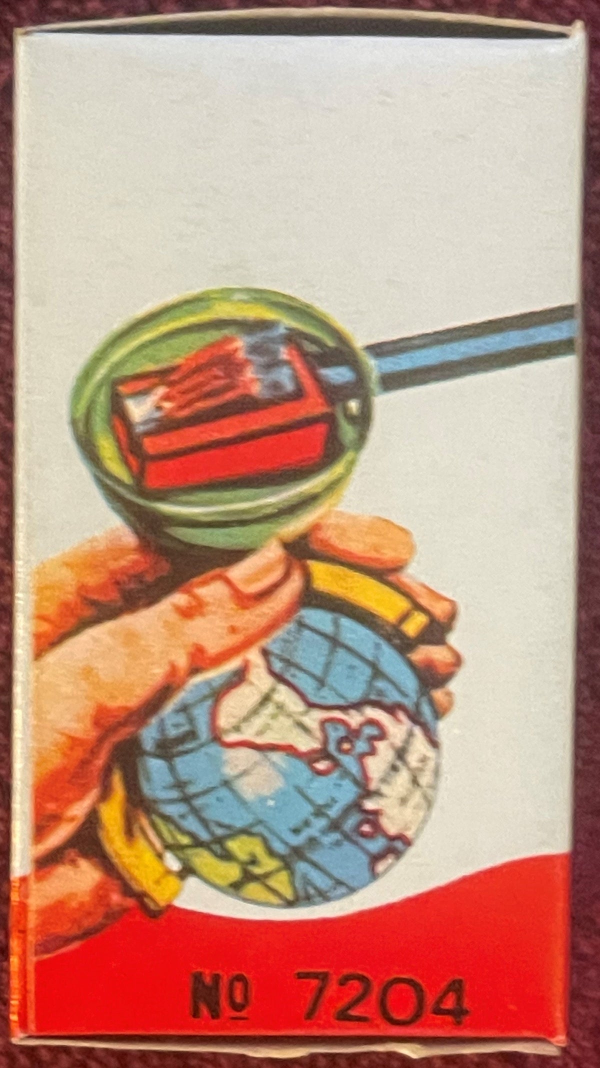Box side panel: an illustrated hand holds the sharpener under a magnifying glass while a blue pencil enters it, with “No 7204” below.