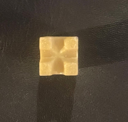 Cream-colored square wax box with embossed cross design, centered on dark textured background