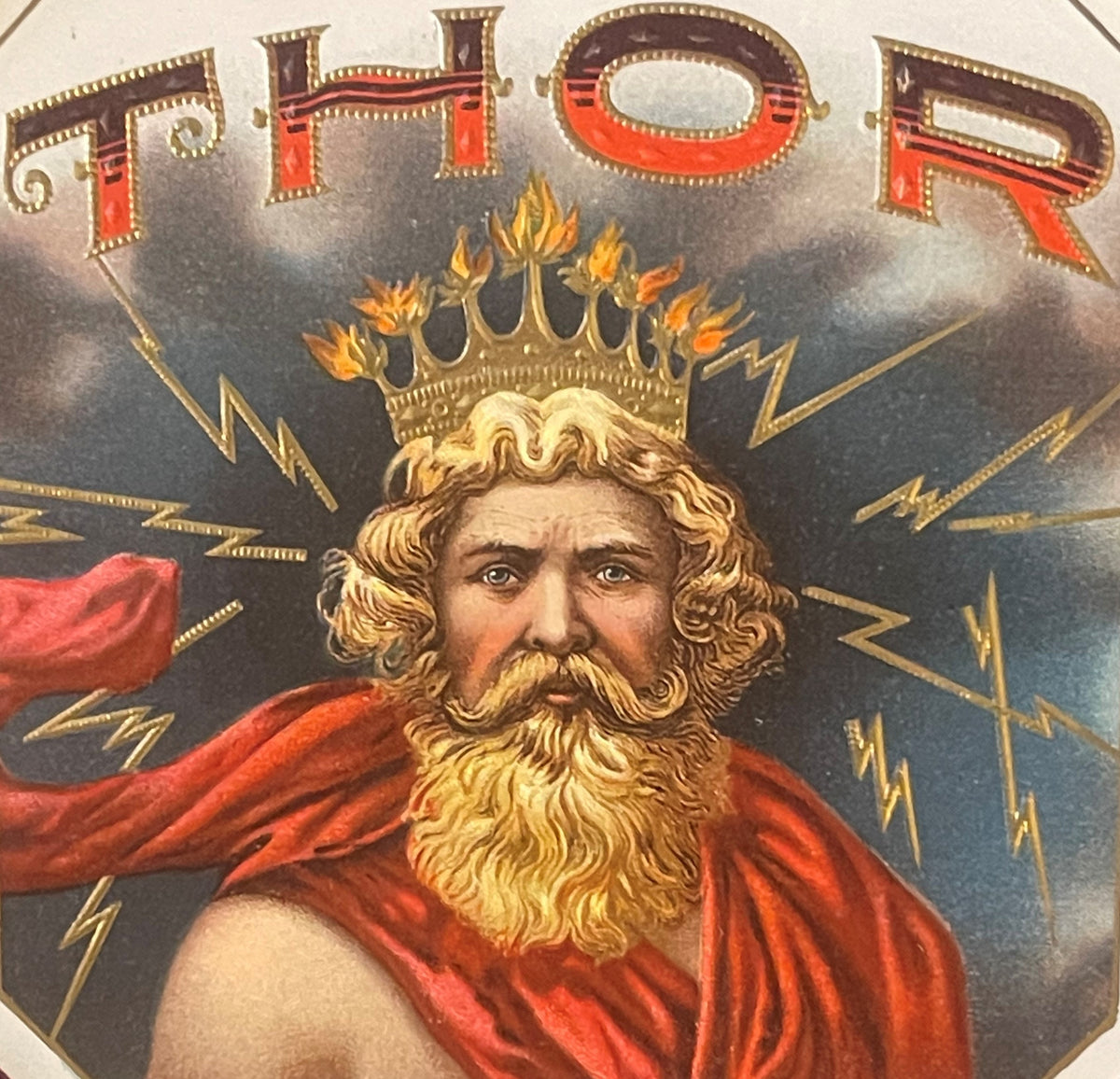 Gold-embossed vintage cigar label featuring bearded man wearing red cape and flaming crown with "THOR" text above, lightning 