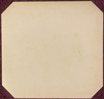 Blank cream-colored vintage cigar label with rounded corners on burgundy fabric background, showing age spots and patina