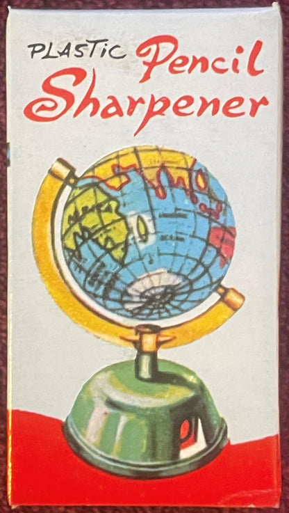 Box front reading “PLASTIC” in black block caps and “Pencil Sharpener” in red script, over an illustration of a globe with a yellow meridian and a green base.