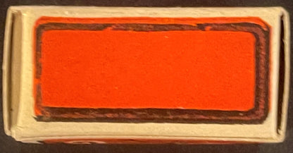 Unopened rectangular box with cream-colored cardboard exterior and bright red/orange label with dark brown border, photograph