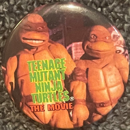 Vintage TMNT button pin featuring two orange cartoon turtles with "Teenage Mutant Ninja Turtles The Movie" text in green and 