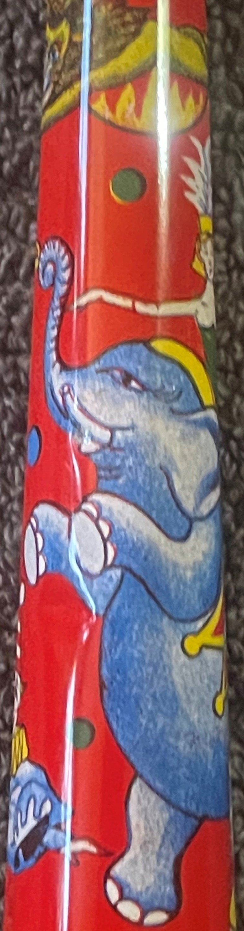Vintage tin horn noisemaker with red background and blue elephant with yellow accents, shown vertically against gray fabric.