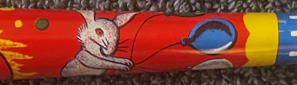 Close-up of red tin horn noisemaker showing white cat in red outfit with blue circular window detail and yellow end cap