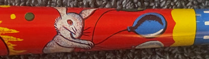Close-up of red tin horn noisemaker showing white cat in red outfit with blue circular window detail and yellow end cap
