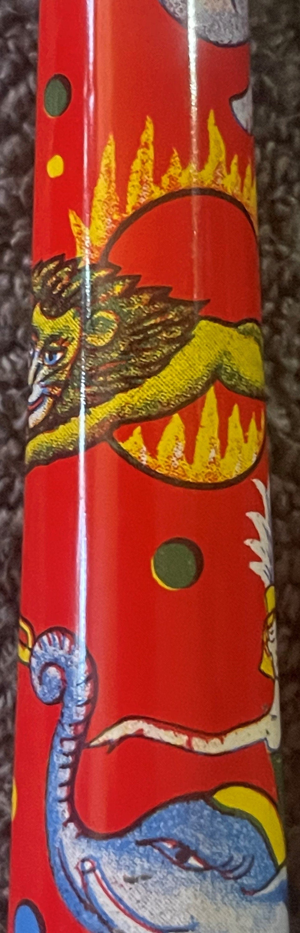Close-up of red tin horn noisemaker showing colorful lithographed circus animals including a winged dragon, blue serpent, and
