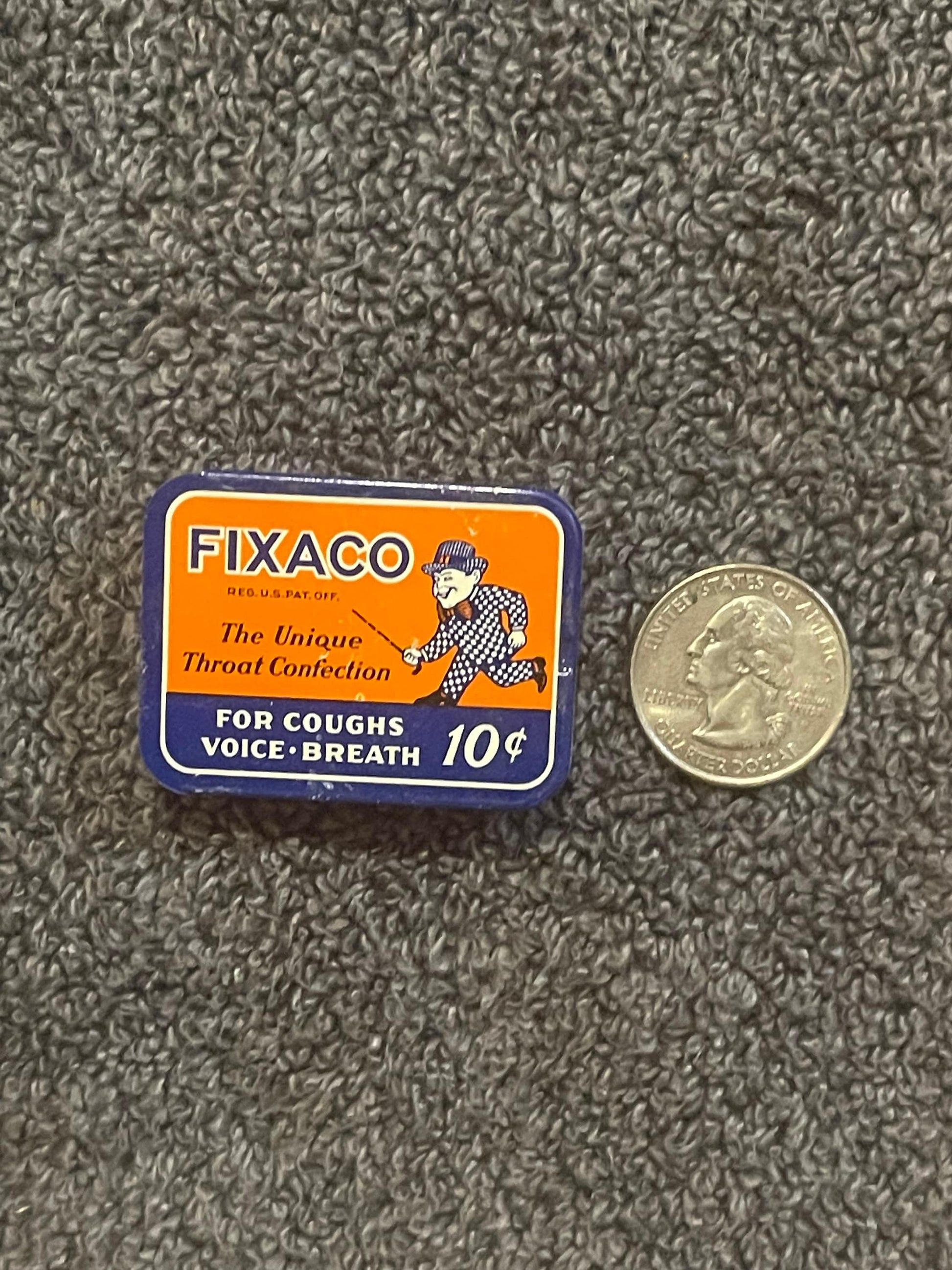 A FIXACO tin photographed beside a US quarter for scale, the coin about as wide as the tin is deep.