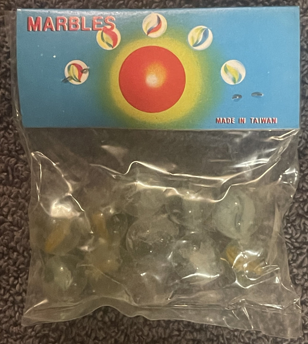 Unopened package of marbles with blue cardboard header showing red central sphere surrounded by eight colorful striped