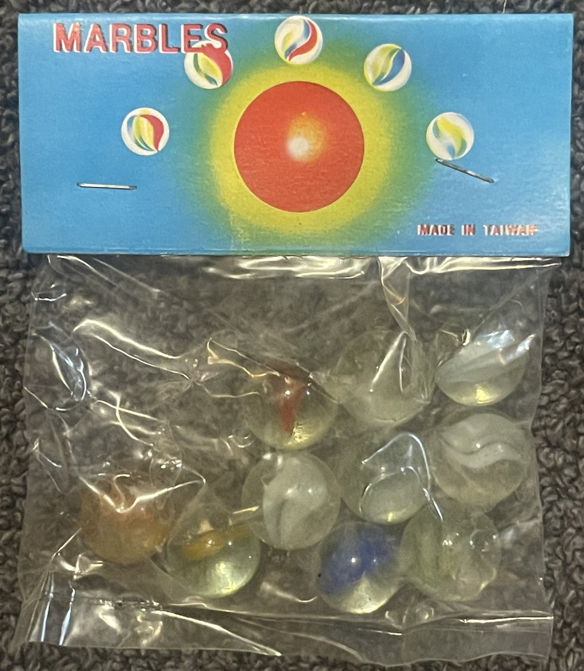 Unopened vintage marbles package with blue box showing red sun and colorful marbles, clear plastic bag containing translucent