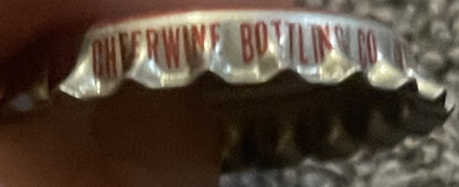 Close-up of vintage bottle cap with red and white ridged edges, showing partial red text reading "CHEERWINE BOTTLING CO" on c