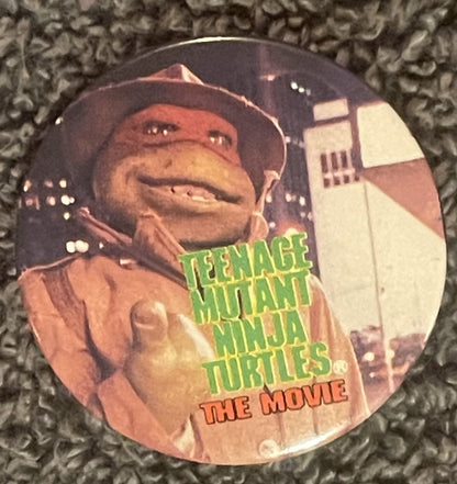 Vintage TMNT movie pin featuring a cowboy turtle character giving thumbs up, with green text on textured fabric background