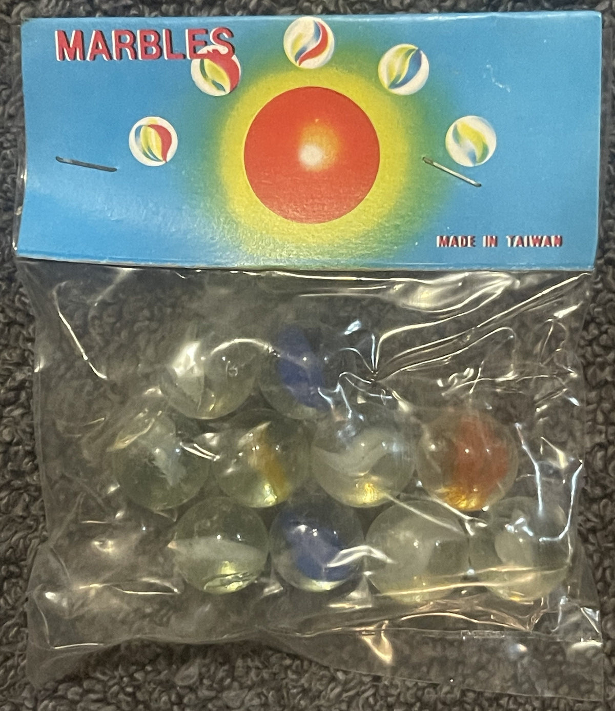 Unopened package of marbles with blue box showing red sphere surrounded by yellow glow and smaller marbles, marked "Made in T