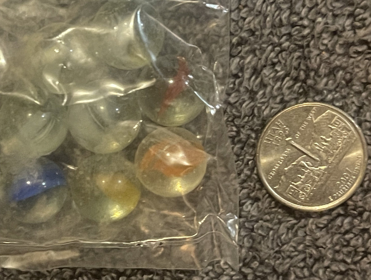 Unopened plastic bag of translucent marbles in yellow, clear, and blue tones, displayed next to a British coin for scale on t
