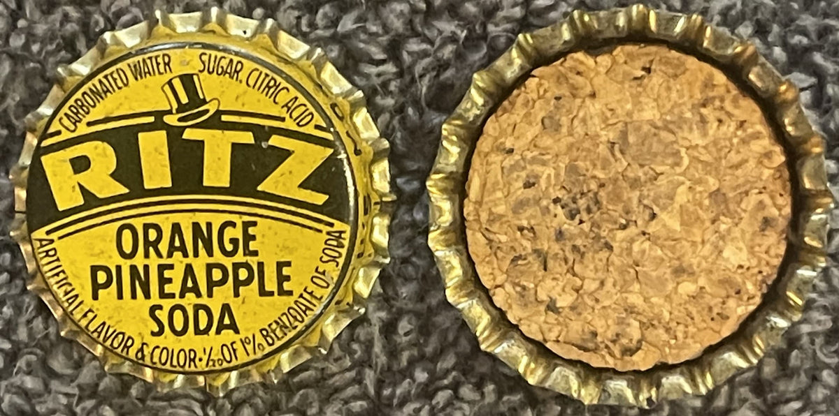 Antique Ritz Orange Pineapple Soda bottle cap, yellow and black printed side showing carbonated water, sugar, citric acid text and top hat logo; reverse side shows cork backing.