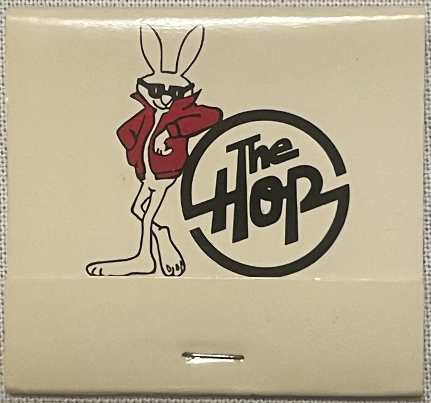 Vintage matchbook cover featuring anthropomorphic rabbit in red jacket next to circular "The Hop" logo text on cream backgrou