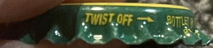 Vintage green and gold twist-off bottle cap with "TWIST OFF" and "BOTTLE" text visible, shown at an angle against a textured 