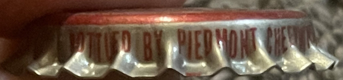 Close-up of vintage metal bottle cap with red and white coloring showing embossed text, viewed from above at an angle