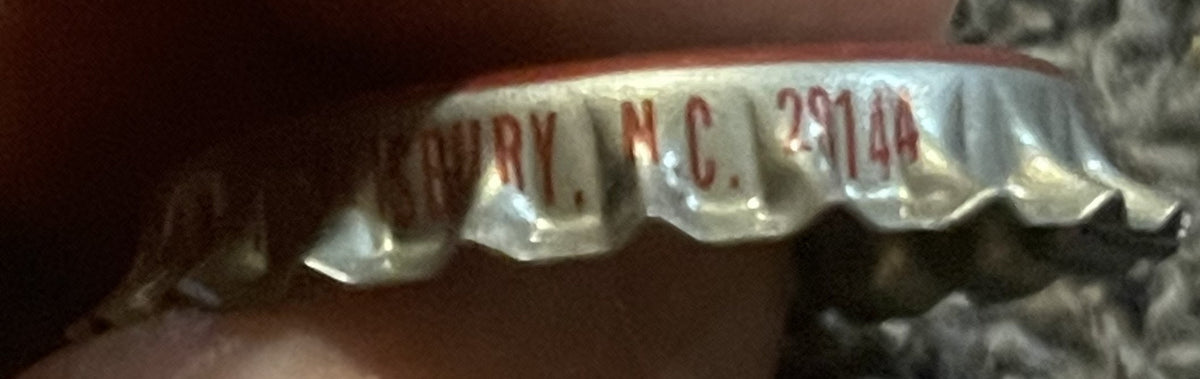 Close-up of vintage bottle cap showing red and white ridged metal with partial text reading "ARRY", "N.C." and "291 14