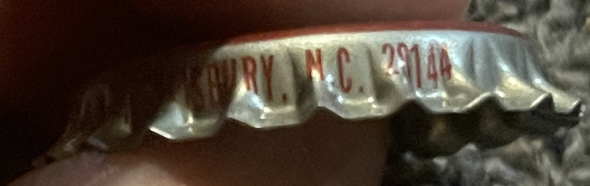 Close-up of vintage bottle cap showing red and white ridged metal with partial text reading "ARRY", "N.C." and "291 14
