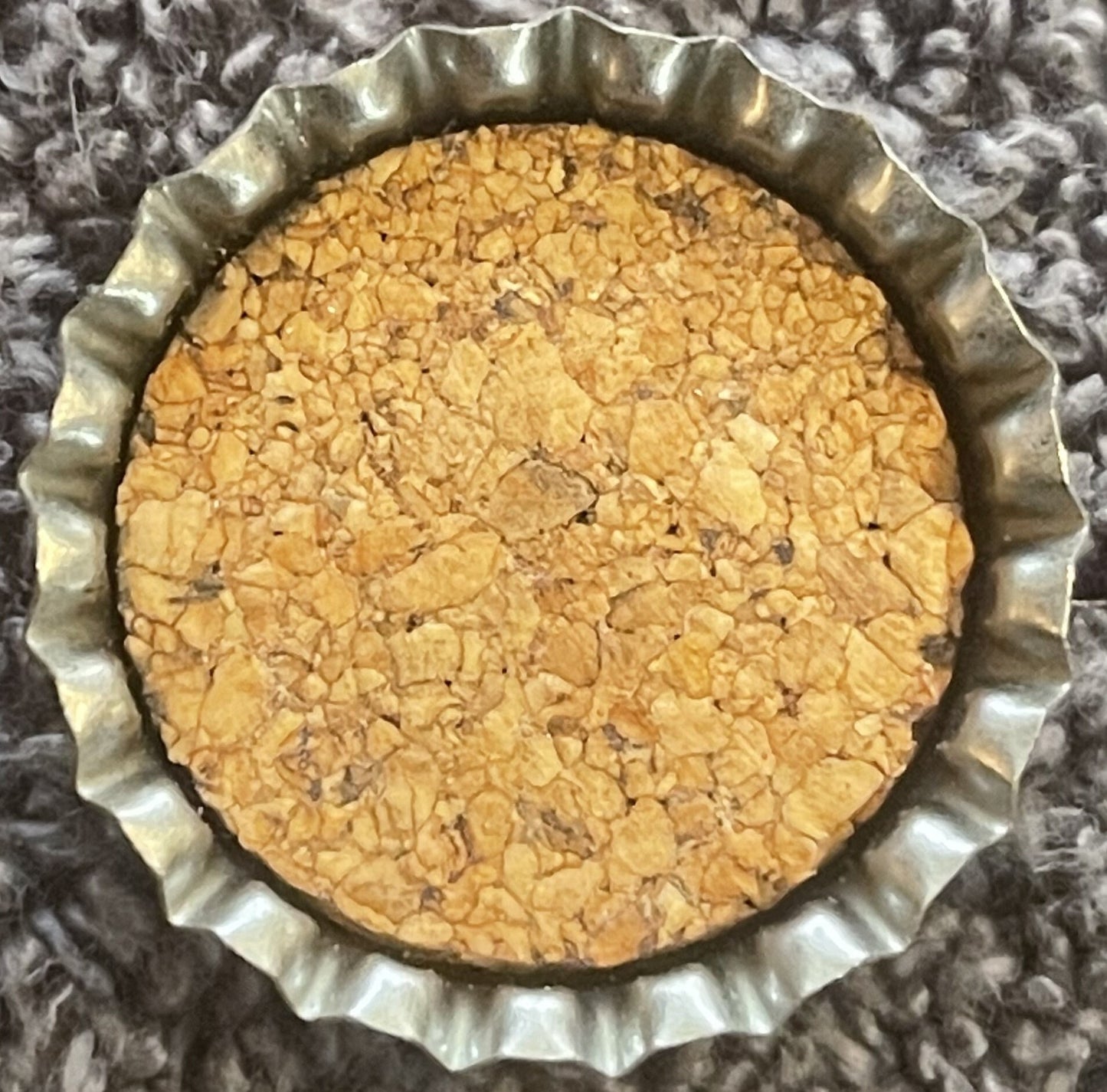 Overhead view of a round tart or pie with a golden crumbly topping in a fluted metal pan on a gray textile background