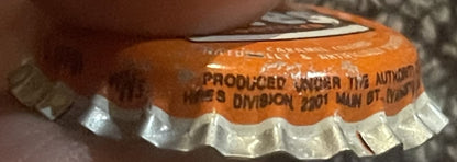 Close-up of orange and white cork bottle cap with embossed text, held by a person's hand for scale