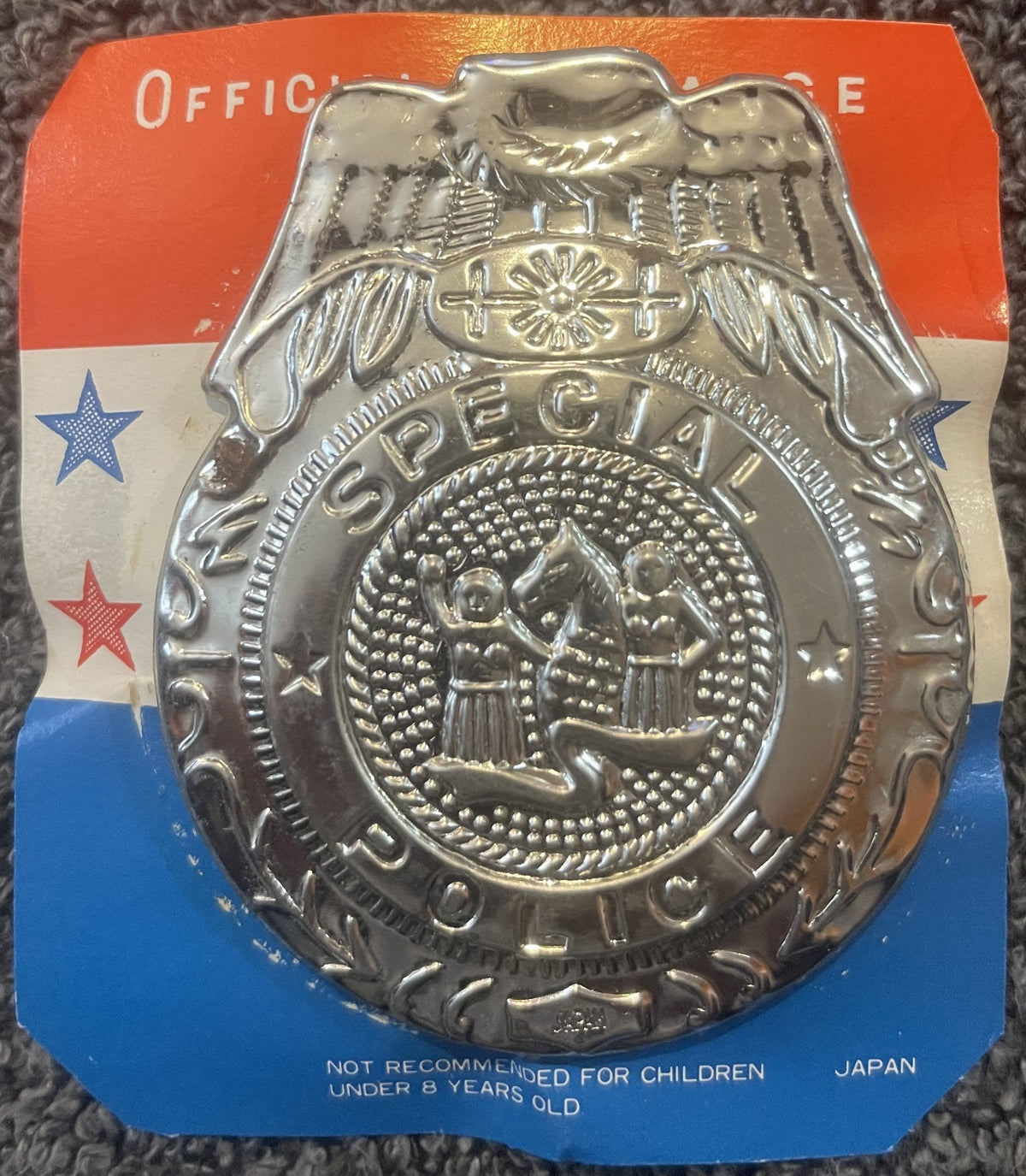 Vintage silver-tone metal police badge with eagle and shield design on red, white and blue cardstock backing, made in Japan.
