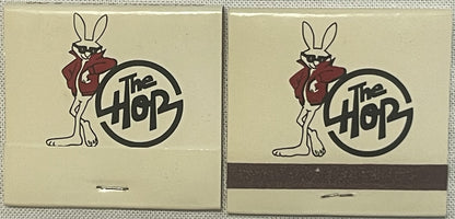 Two vintage The Hop nightclub matchbooks with cartoon rabbit logo in red jacket and circular text design on cream background