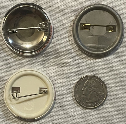 Four button pin backs shown front and back with a quarter for scale, including two metal pin mechanisms and two plastic backi