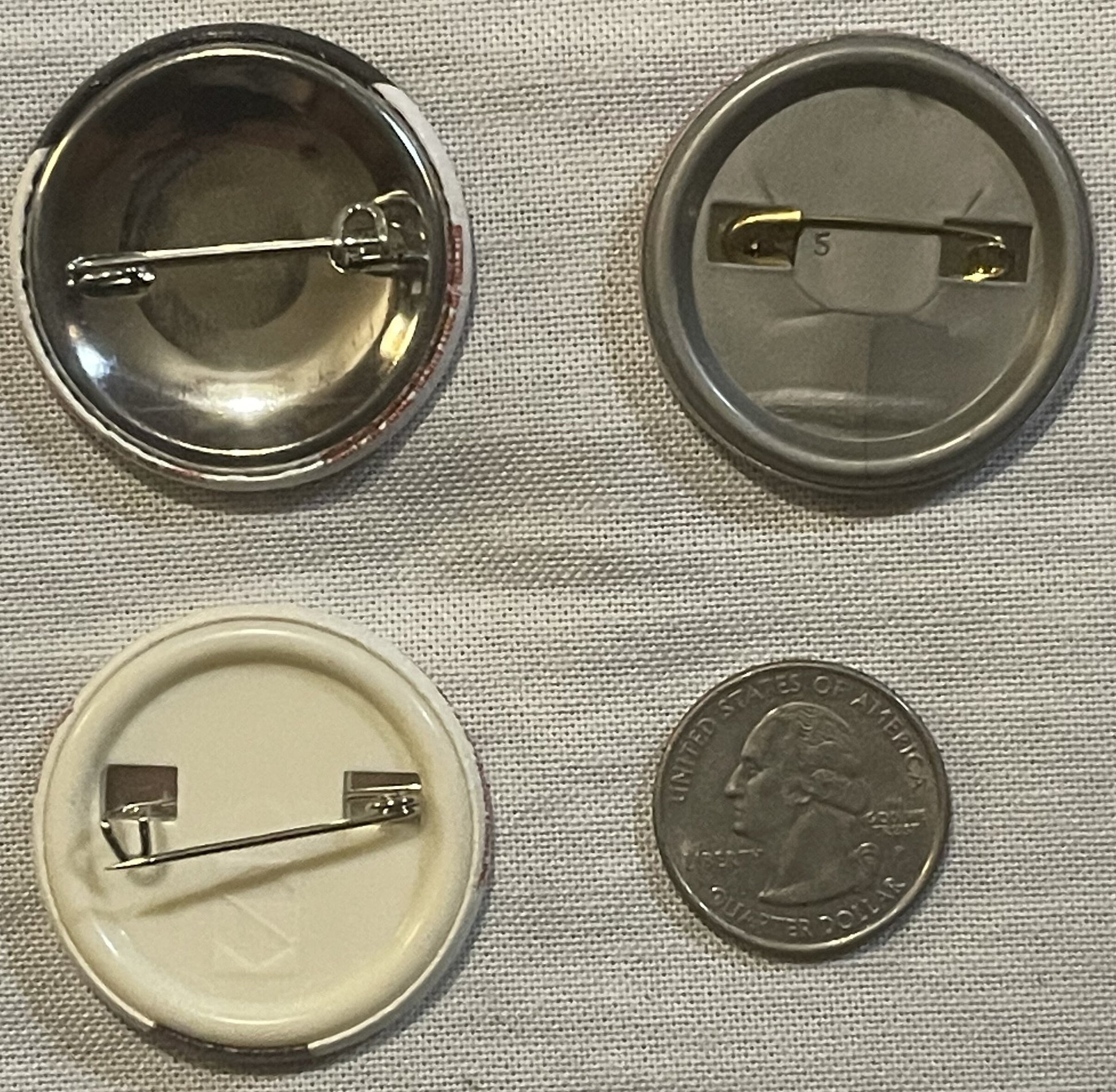 Four vintage pin-back buttons shown front and back with a quarter for scale; top two metal with eyeball designs, bottom two p