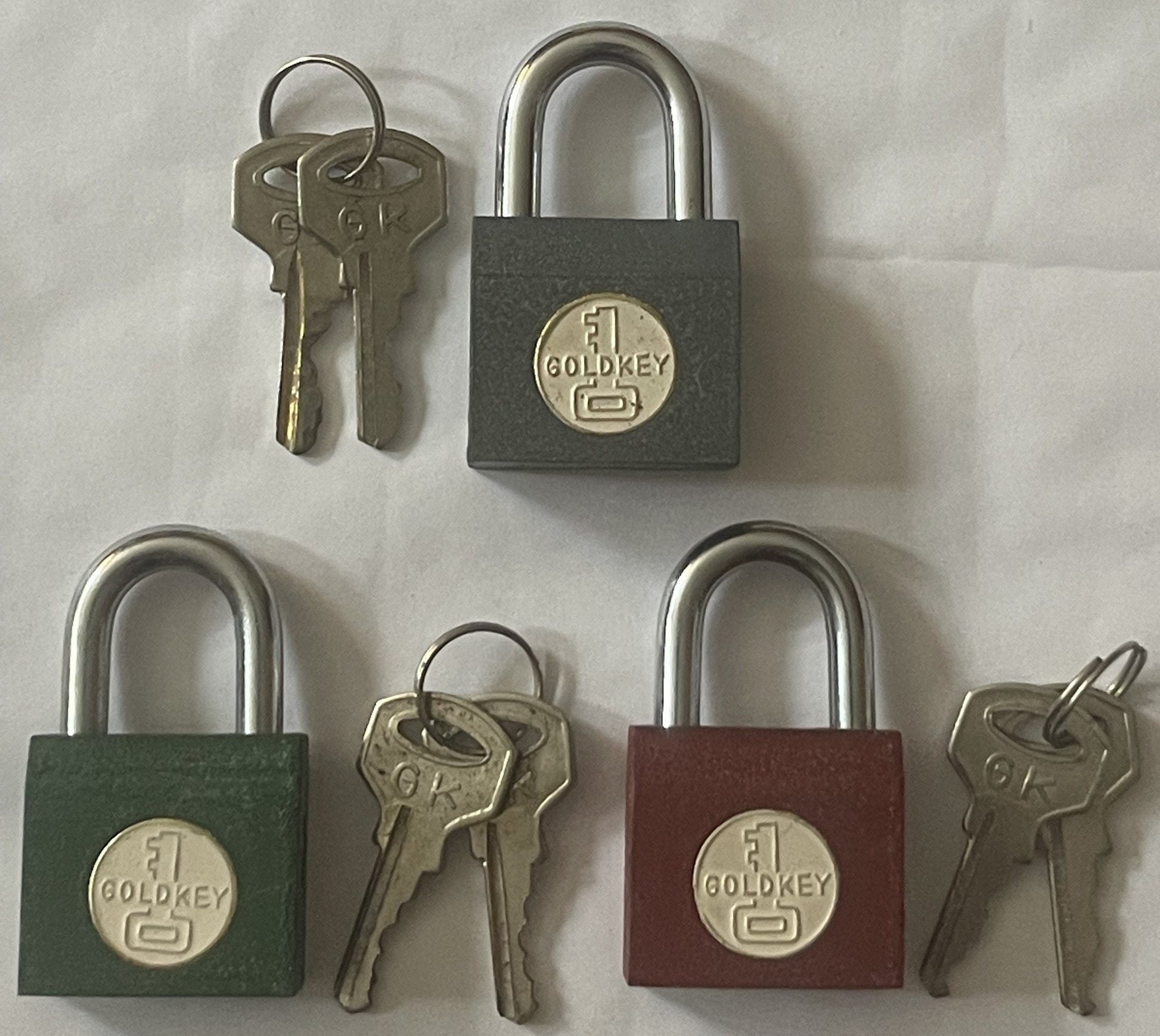 Three vintage GoldKey padlocks in gray, green, and burgundy with matching brass keys displayed on white background