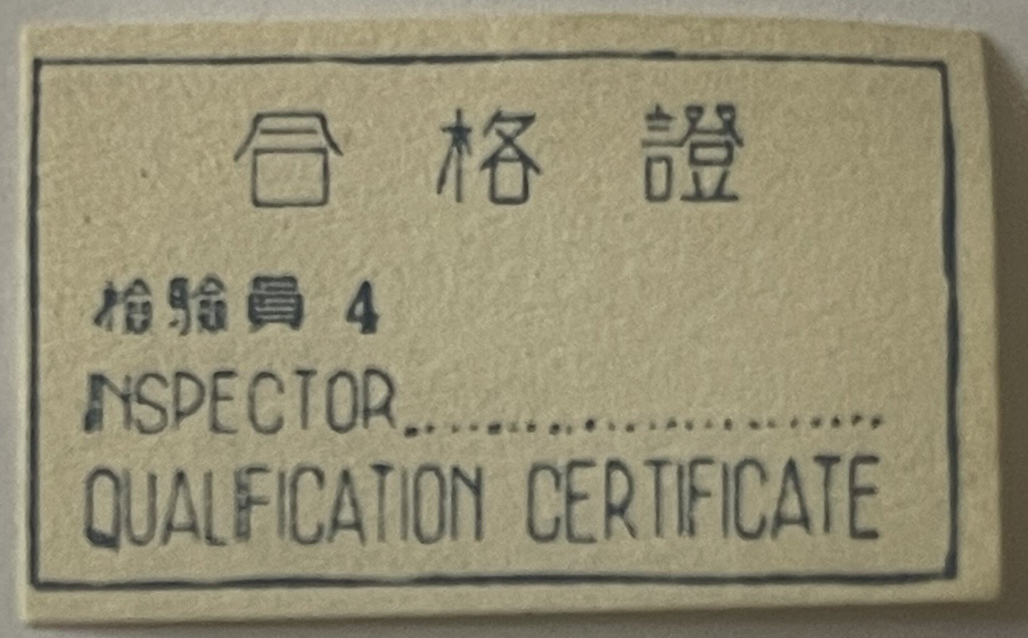 Cream-colored metal tag with embossed Chinese characters and English text reading "INSPECTOR QUALIFICATION CERTIFICATE
