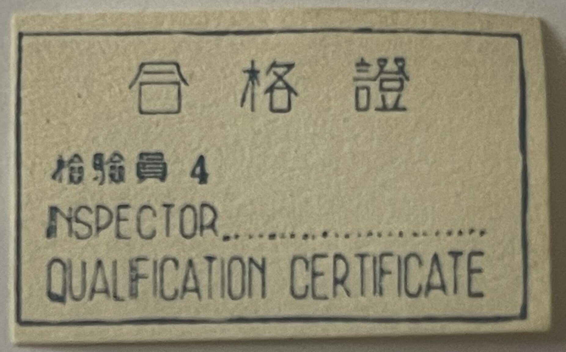 Cream-colored metal tag with embossed Chinese characters and English text reading "INSPECTOR QUALIFICATION CERTIFICATE