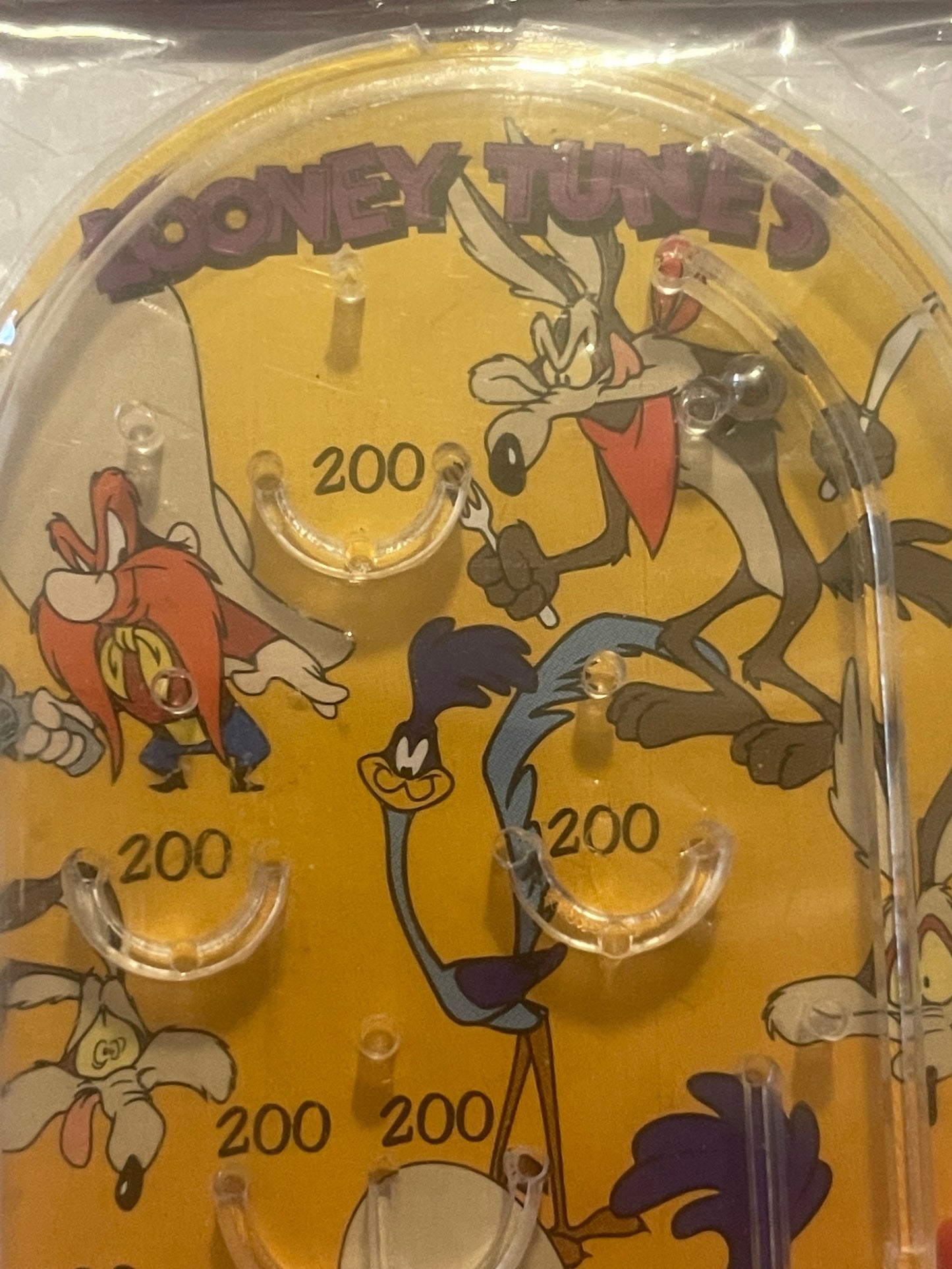 Amber-colored mini pinball playfield with Looney Tunes characters including Bugs Bunny, Wile E Coyote, and Road Runner, marke