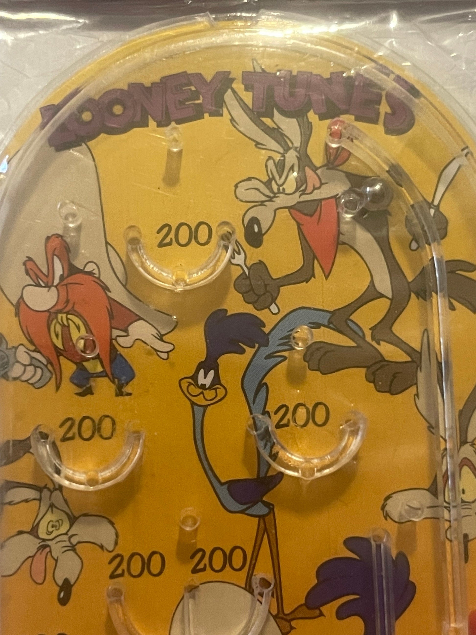 Amber-colored mini pinball playfield with Looney Tunes characters including Bugs Bunny, Wile E Coyote, and Road Runner, marke