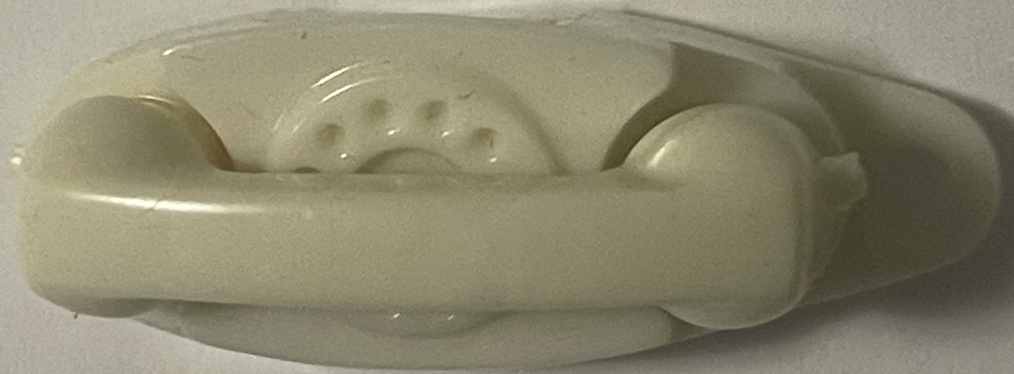 Overhead view of cream-colored plastic vintage telephone keychain showing rotary dial detail and handset, cast against white 