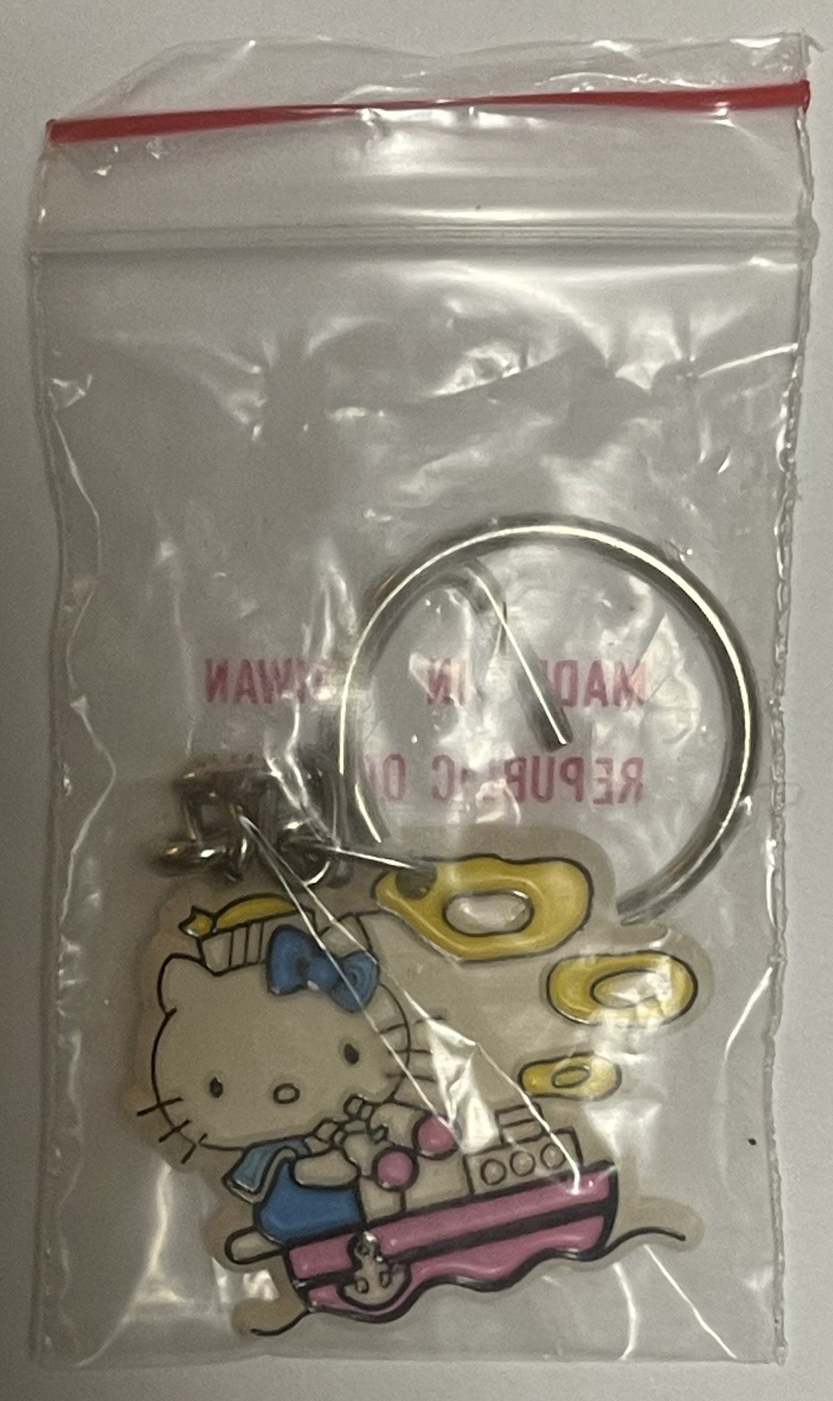 Hello Kitty sailor boat keychain in original plastic packaging with red zipper seal, showing character in blue outfit playing