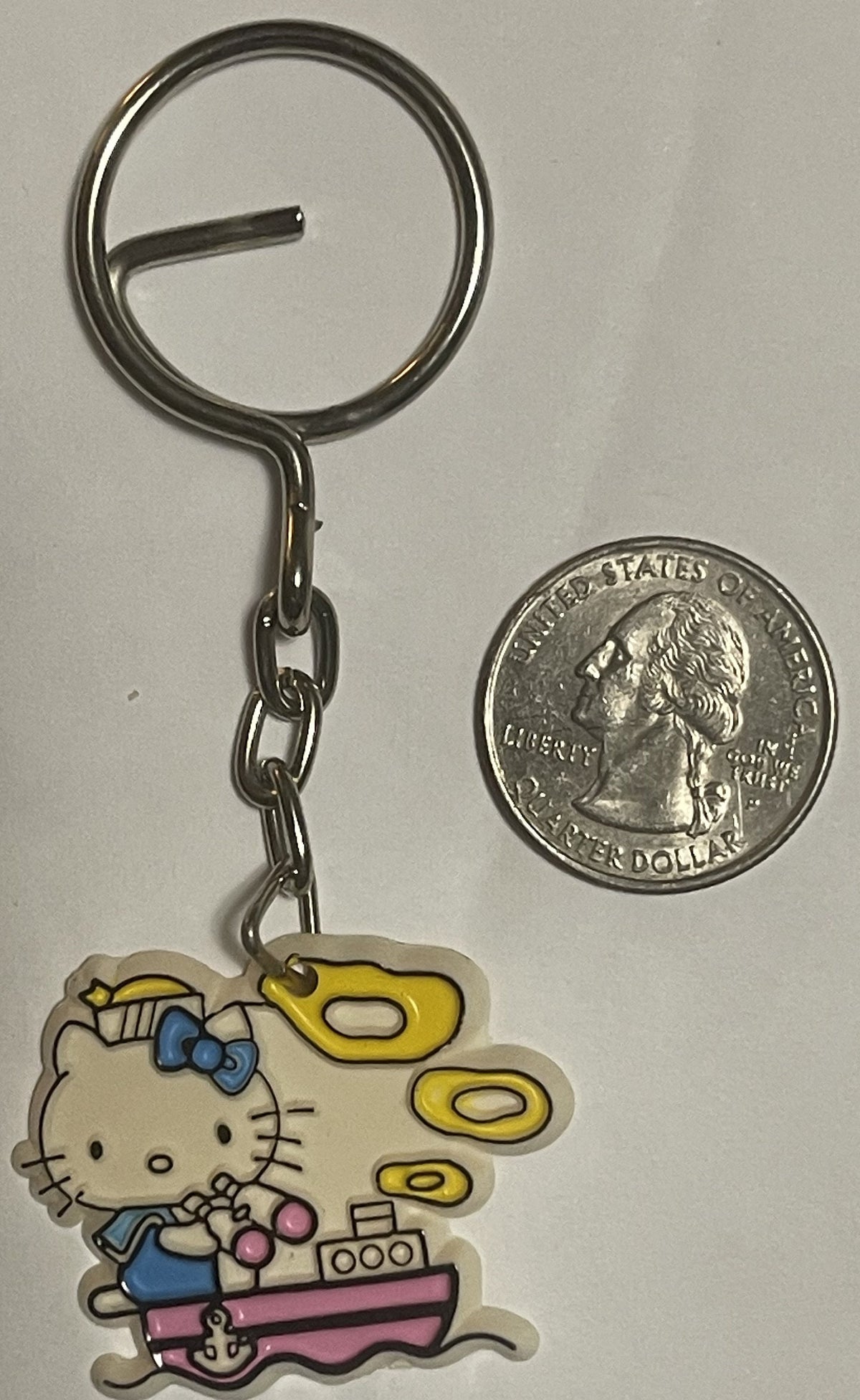 Vintage Hello Kitty sailor boat keychain with blue bow and yellow sail next to US quarter for scale