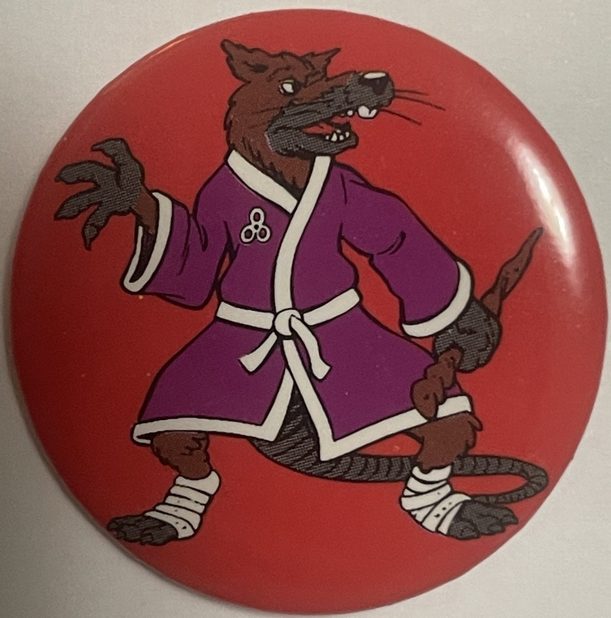 Round red pinback button featuring cartoon Splinter character in purple robe with white trim, brown fur, and clawed hands