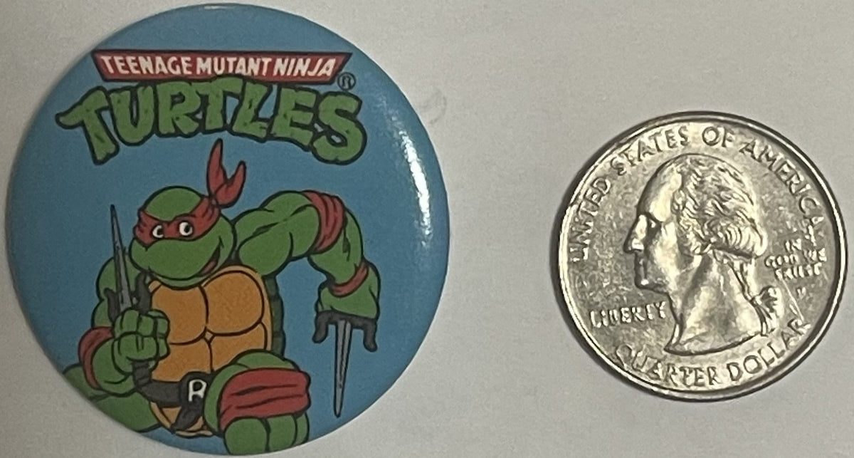 Vintage TMNT pinback button featuring Raphael in red mask holding swords, next to a US quarter for scale