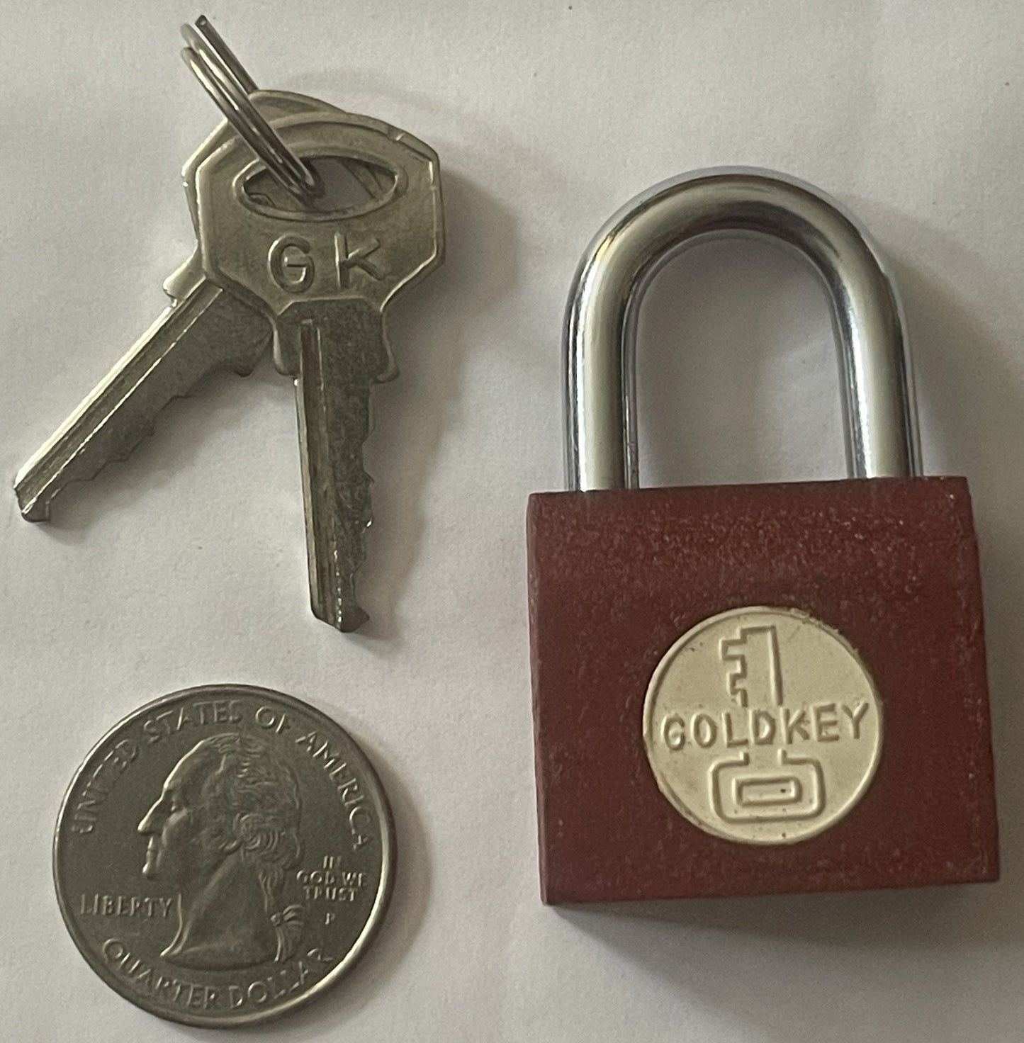 Vintage GoldKey padlock with red body and silver shackle, displayed with matching key and US quarter for scale