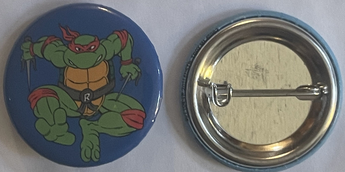 Front and back of a blue pinback button featuring a green Teenage Mutant Ninja Turtle with red mask and "R" on chest, shown