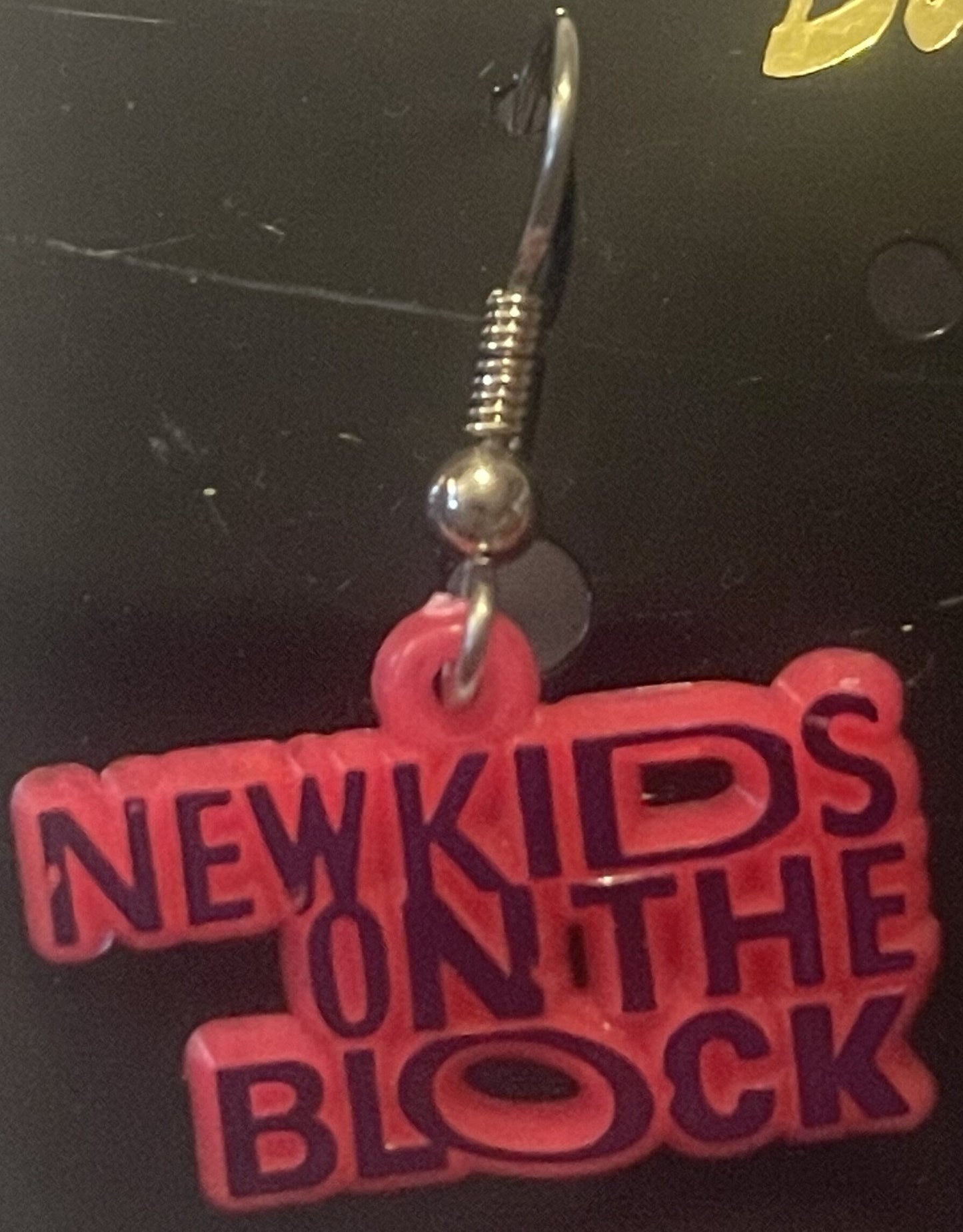Red "New Kids on the Block" logo charm with metal hook and ball connector against dark background