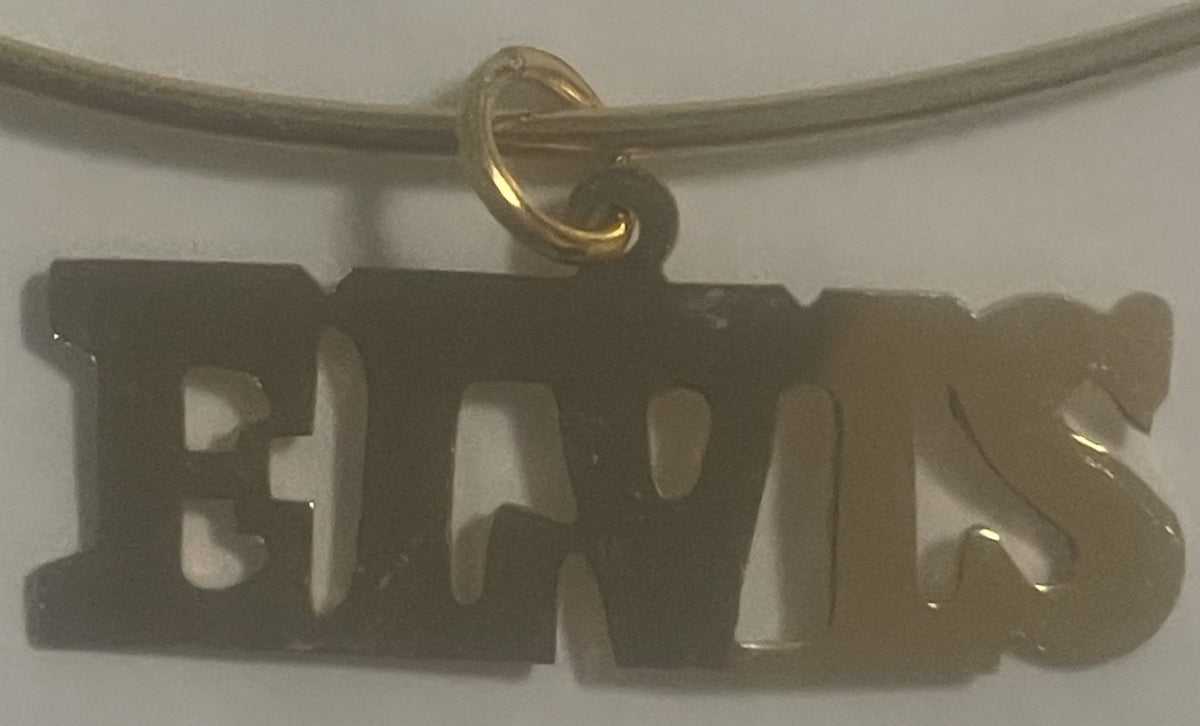 Gold-tone "ELVIS" nameplate charm hanging from a metal chain against a white background