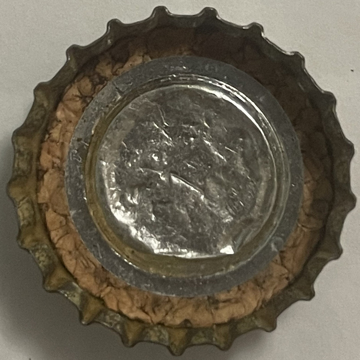 Vintage metal bottle cap with scalloped edges, showing embossed portrait profile and text, centered on white background with 