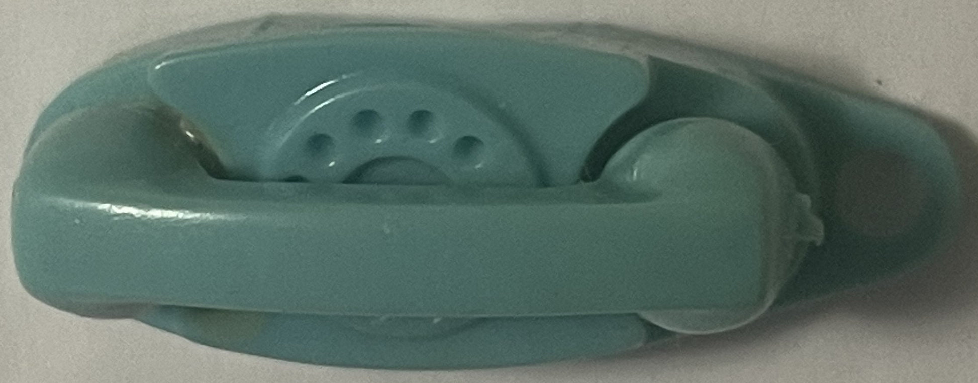 Teal plastic vintage telephone keychain charm shown from above against white surface, displaying rotary dial and handset deta