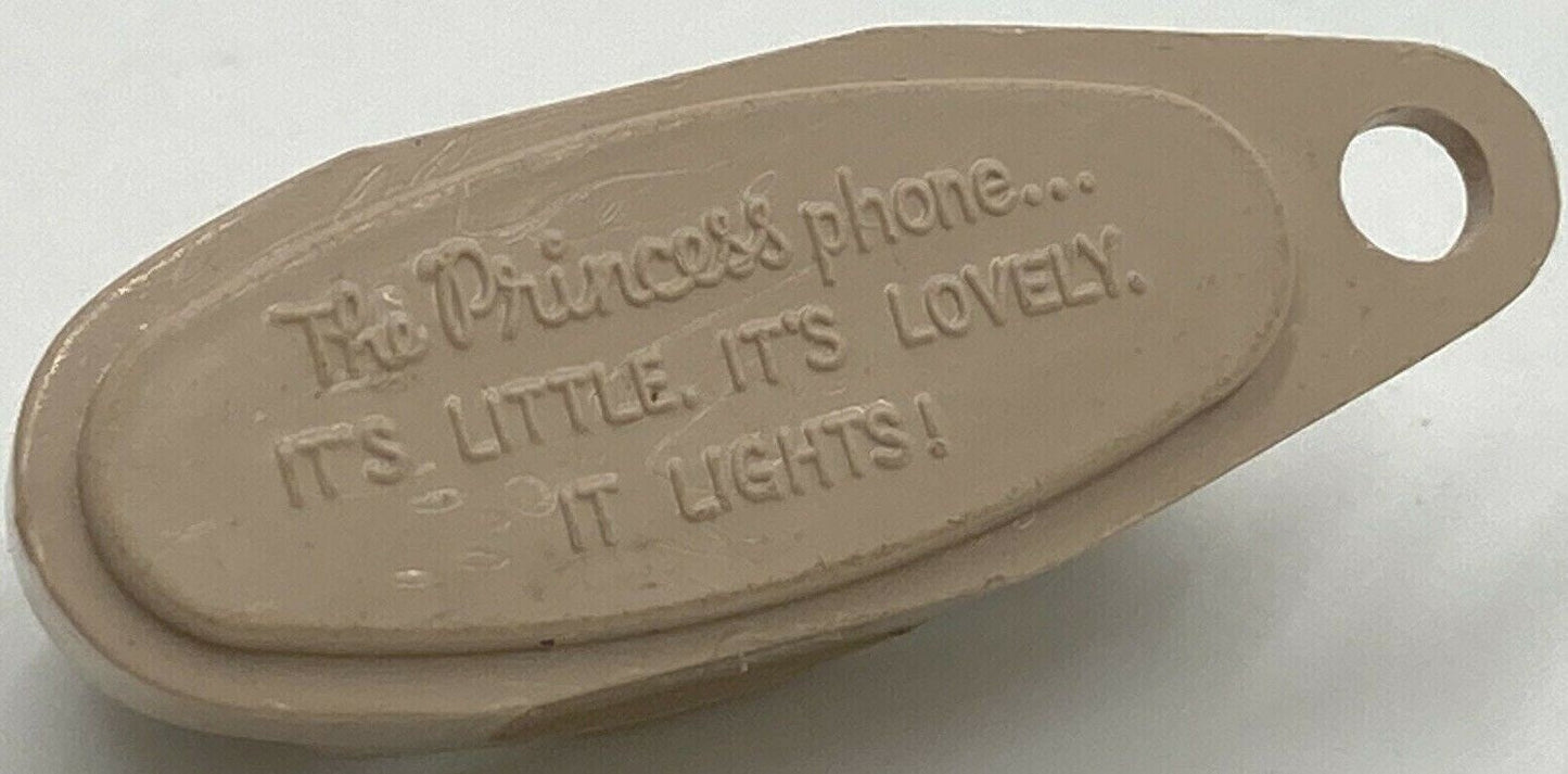 Beige plastic phone keychain with embossed text reading "The Princess phone... It's Little. It's Lovely. It Lights!" shown at
