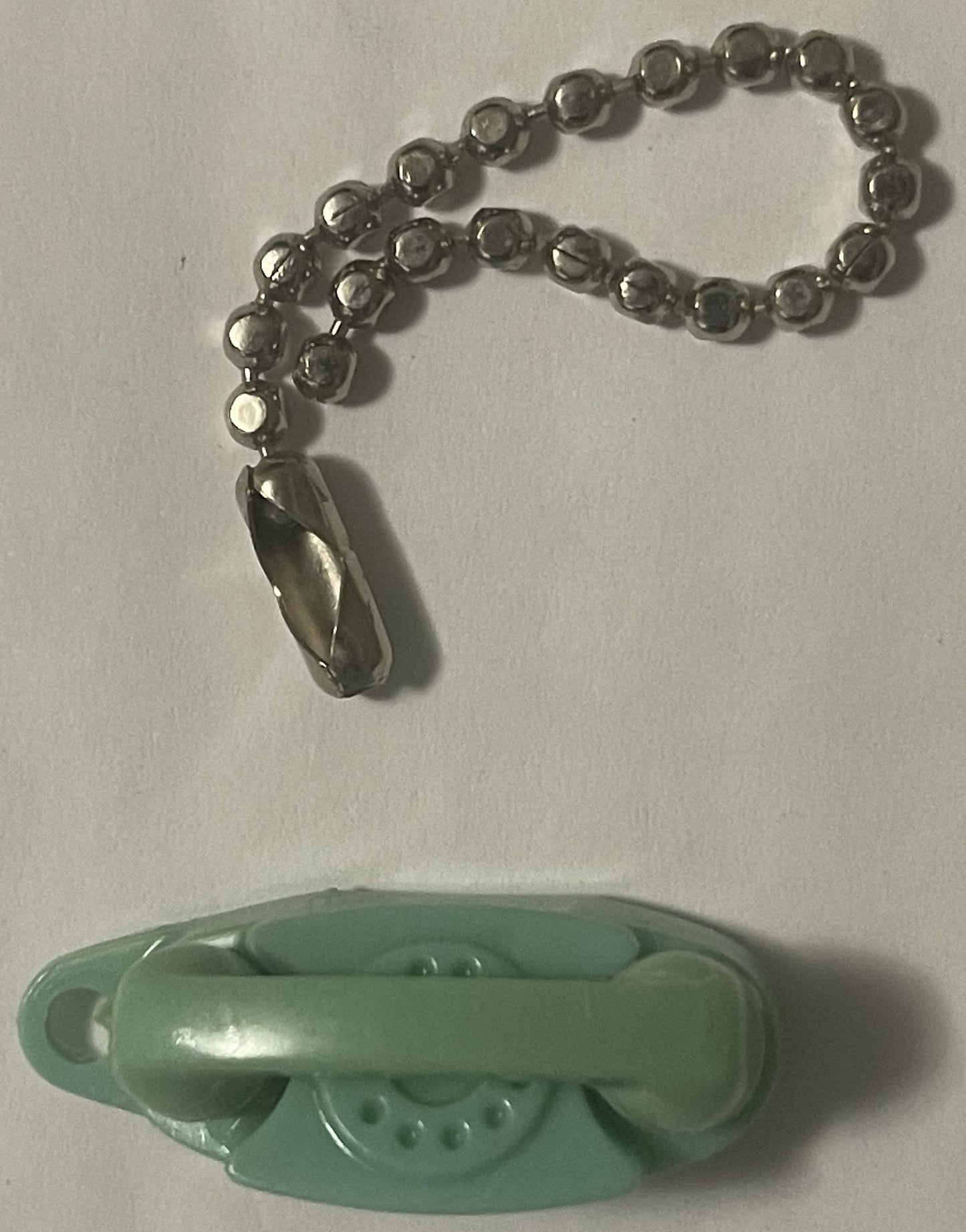 Vintage green plastic rotary phone keychain with metal beaded chain and teardrop charm, displayed above matching phone base o